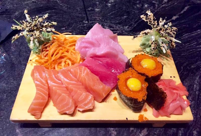 A wooden board with sushi and other food on it.